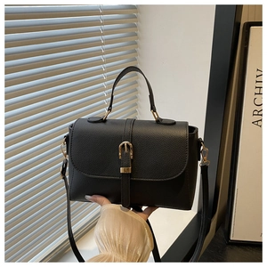Close-up of black lychee grain texture with gold buckle detail on crossbody bag