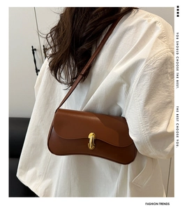 Détail d'un sac hobo marron avec fermoir doré porté sur un manteau blanc