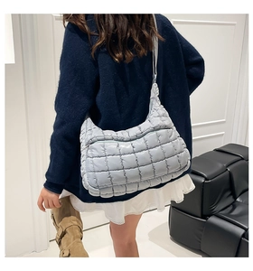 Rear view of a light blue quilted down crossbody bag on a model in a minimalist room