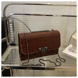 Detail of dark brown crocodile texture flap bag with metallic chain and buckle clasp