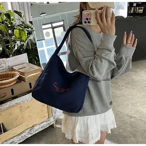 Deep blue canvas tote bag with red embroidered text shown on model in a casual setting