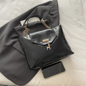 Chic black shiny tote bag with gold chain and deer pendant on grey blazer background