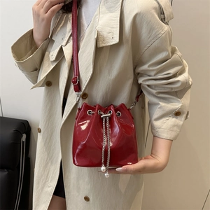 Chic red patent leather bucket bag with silver chain and pearl charms worn by a model