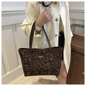 Detail of leopard print tote bag with brown handles and golden brand plaque on front