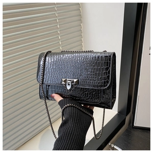 Detail of black crocodile pattern handbag featuring a metal chain and lock buckle strap
