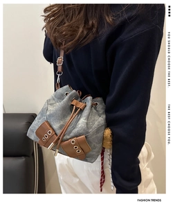 Detail of grey denim bucket bag featuring brown leather straps and drawstring closure