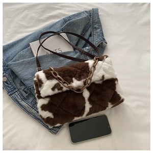 Vue à plat d'un sac à bandoulière en peluche motif vache avec chaîne et sangle en cuir