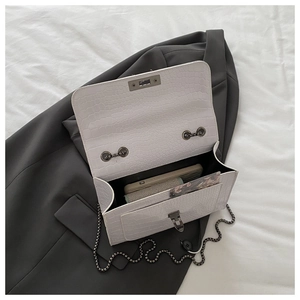 Detail view of white croc-embossed flap bag interior with silver chain strap and metal lock