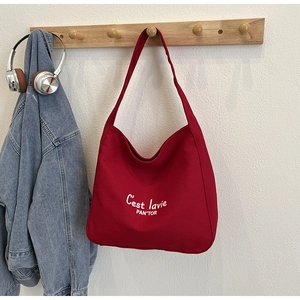Détail d'un sac cabas en toile rouge avec lettrage blanc suspendu à un crochet en bois