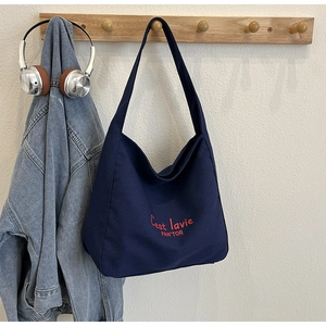 Détail du sac cabas en toile marine avec broderie rouge suspendu à un crochet mural