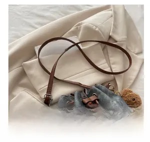 Detail of denim bucket bag showing brown leather strap and cute plush bear charm