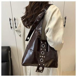 Detalle de bolso tote de charol marrón oscuro con ojales metálicos plateados