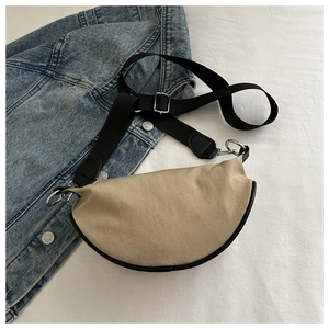 Détail d'un sac bandoulière demi-lune en toile beige avec bordure noire et sangle large