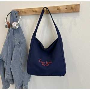 Détail d'un cabas en toile bleu marine avec broderie rouge sur crochet en bois