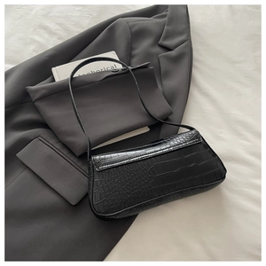 Close-up of black crocodile embossed baguette bag styled on a grey blazer suit