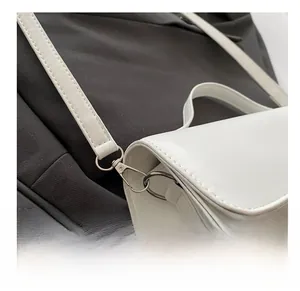 Close-up of silver metal swivel hook and fine stitching on white PU leather bag strap