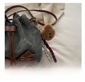Close-up of denim bucket bag with brown leather drawstring and plush bear charm