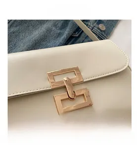 Close-up of white leather crossbody bag with polished gold-tone interlocking metal buckle