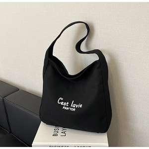 Détail du sac cabas en toile noire avec lettrage blanc posé sur un support élégant
