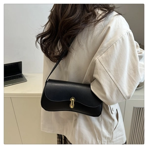 Détail d'un sac d'épaule en cuir noir avec fermoir rotatif doré porté par un modèle