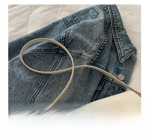 White leather crossbody bag with metal buckle on denim jacket background detail
