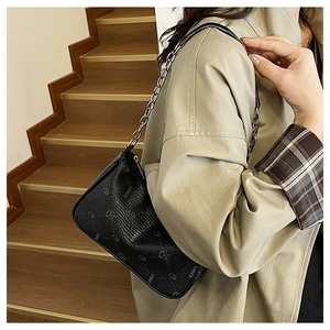 Schwarze Baguette-Tasche mit Litschitextur und Silberkette am beigen Mantel gezeigt