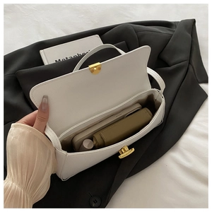 Dettaglio borsa sottospalla in pelle bianca con fibbia dorata su blazer nero