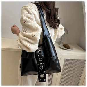Detalle de un bolso Hobo de cuero negro brillante con ojales plateados y remaches estilo punk