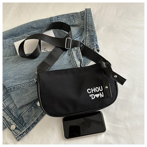 Détail du sac bandoulière noir avec broderie coeur à côté d'un smartphone pour la taille