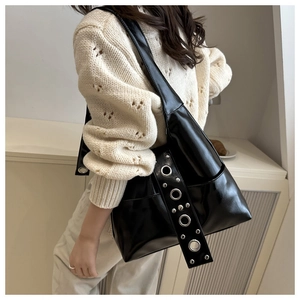 Detalle de bolso tote negro brillante con ojales metálicos y correa ancha