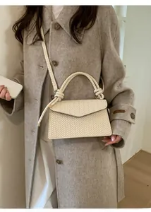 Detail of cream woven crossbody bag with decorative knot handle on a wool coat