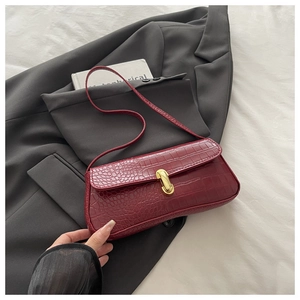 Close-up of burgundy crocodile pattern baguette bag with golden metal clasp detail