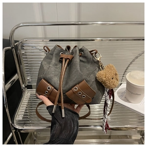 Close-up of canvas bucket bag featuring leather drawstring and plush bear accessory