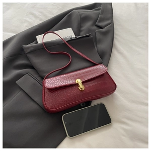 Detail of burgundy crocodile pattern baguette bag with gold metal twist lock and phone