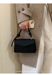 Detailed view of black woven texture handbag with twisted handle and gold hardware links