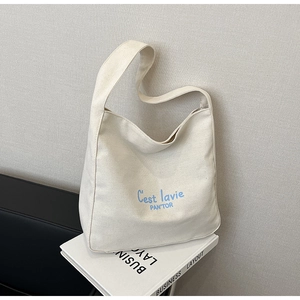 Detail of off-white canvas tote bag featuring light blue text and wide shoulder strap