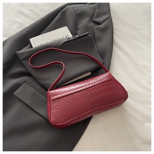Close-up of deep red crocodile pattern baguette bag on a grey blazer with book