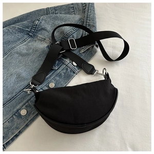 Sac bandoulière en nylon noir en forme de croissant avec sangle réglable sur du denim