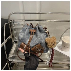 Detail of drawstring bucket bag in blue denim with brown leather straps and bear charm