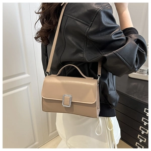 Detail of beige faux leather crossbody bag with silver buckle worn by a model