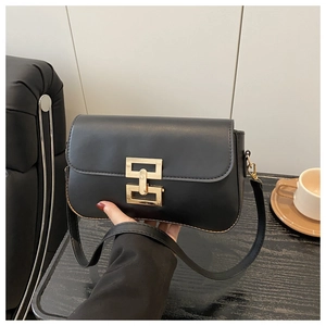 Detail of black crossbody bag with gold interlocking buckle on a minimalist table