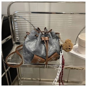 Detailed close-up of denim drawstring bucket bag with leather accents and bear charm