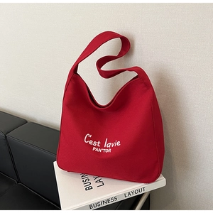 Detail of red canvas hobo bag featuring white C'est la vie PAN'TOR embroidery text