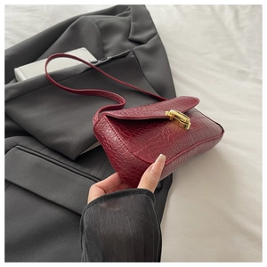 Close-up of wine red faux crocodile skin bag with vintage gold buckle on a black blazer