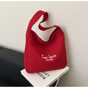 Détail du sac hobo en toile rouge avec lettres blanches posé sur un livre chic