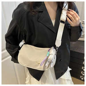 Détail du sac brodé blanc crème avec large bandoulière en tissu porté en travers
