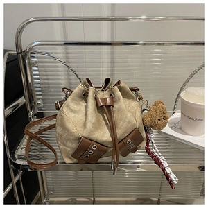 Close-up of khaki canvas drawstring bucket bag with leather pockets and a cute bear charm