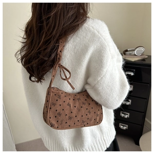 Close-up of brown corduroy crossbody bag featuring black bow and heart patterns