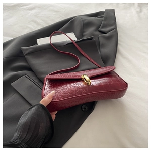 Detail of burgundy crocodile embossed faux leather baguette bag with golden metal twist lock