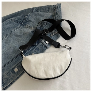 Vue détaillée du sac bandoulière blanc en demi-lune avec bordure noire sur denim